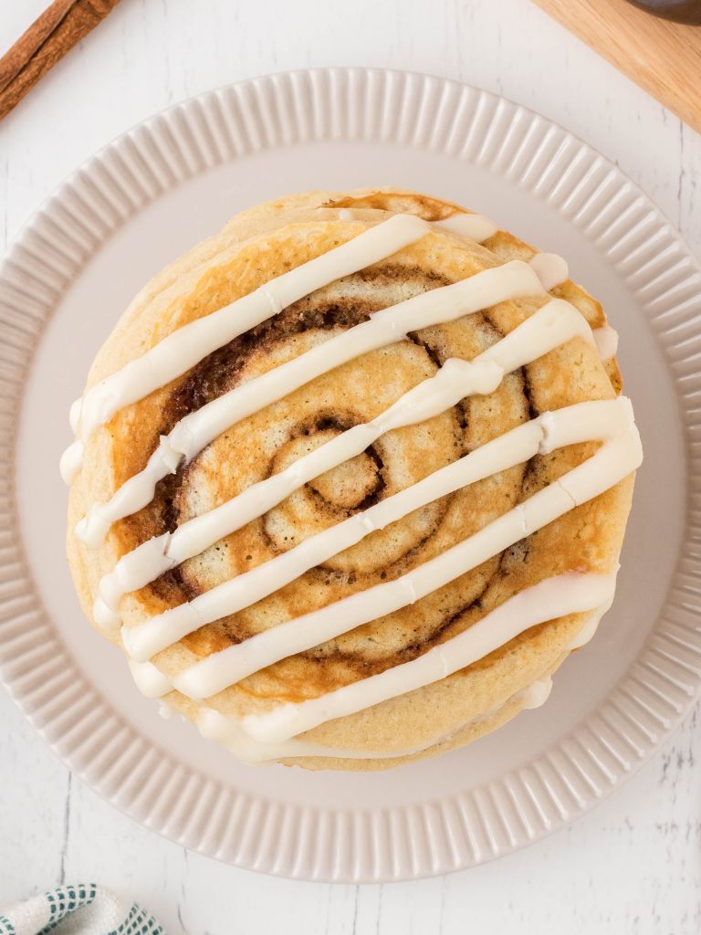 Pancakes on a white plate with a cream cheese glaze over top. 