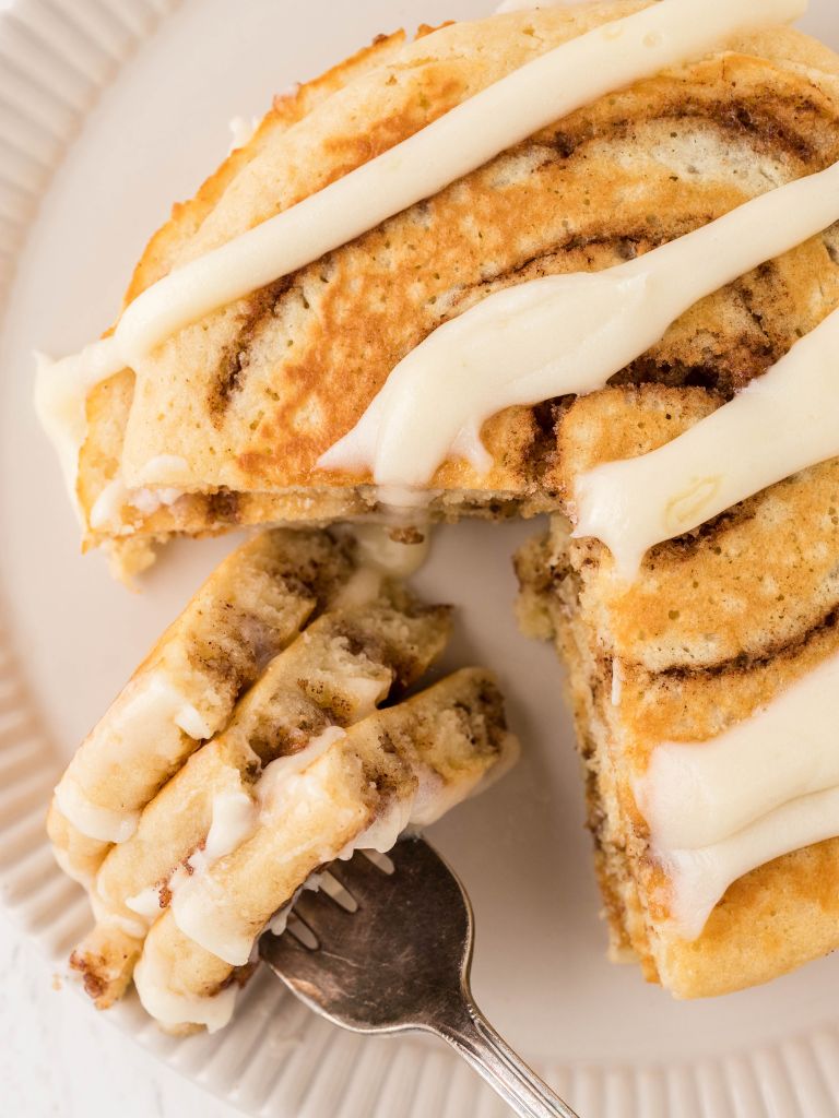 Cinnamon roll pancakes with a fork that has a bite of the stack on it. 
