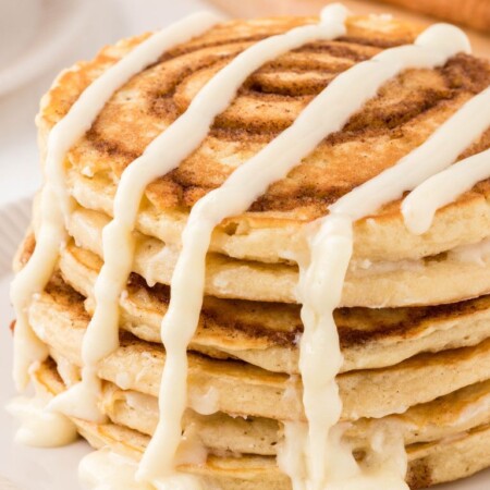Stack of cinnamon swirl pancakes with a cream cheese glaze dripping over it.