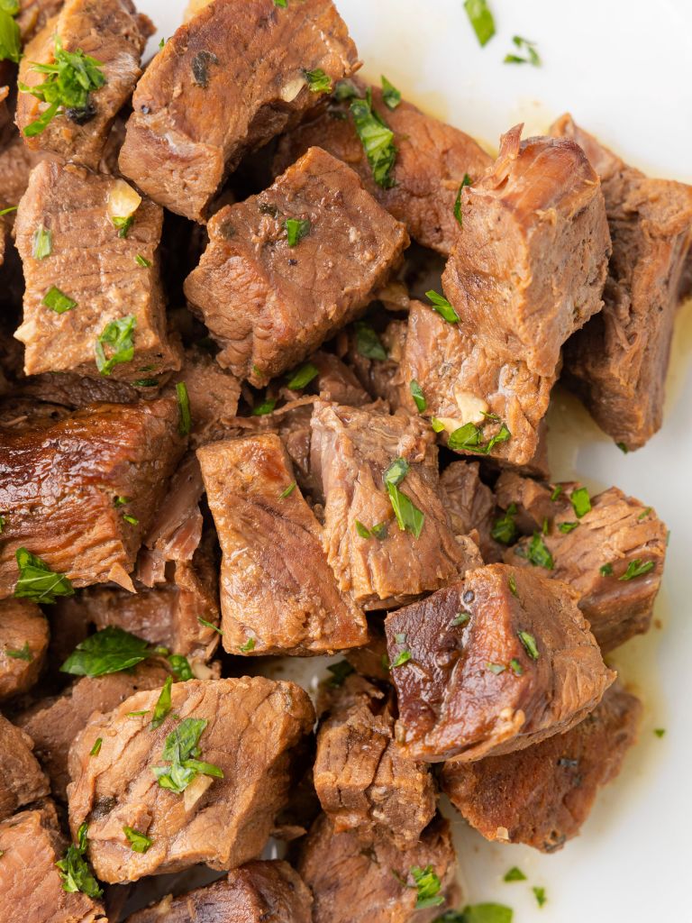 A pile of steak cut into bites garnished with parsley. 
