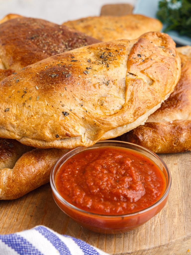 A calzone on a stack of others with a towel next to it and a bowl of sauce. 