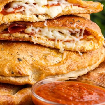 A stack of calzones with cheese dripping out of the top and a bowl of marinara sauce next to it.
