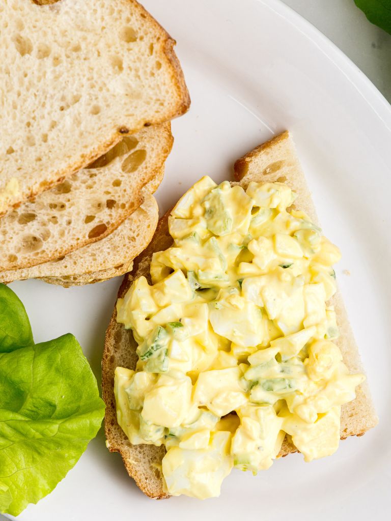 An open faced piece of bread with egg salad on it and a piece of lettuce. 