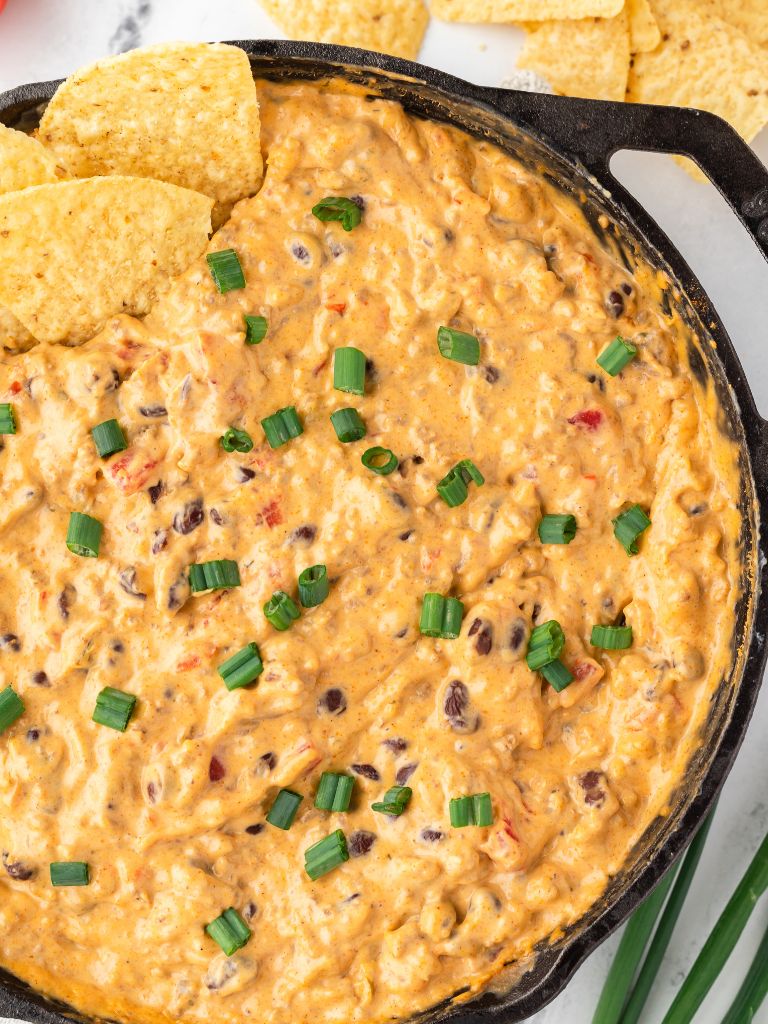 A cast iron skillet filled with a cheesy dip and some chips in the corner.