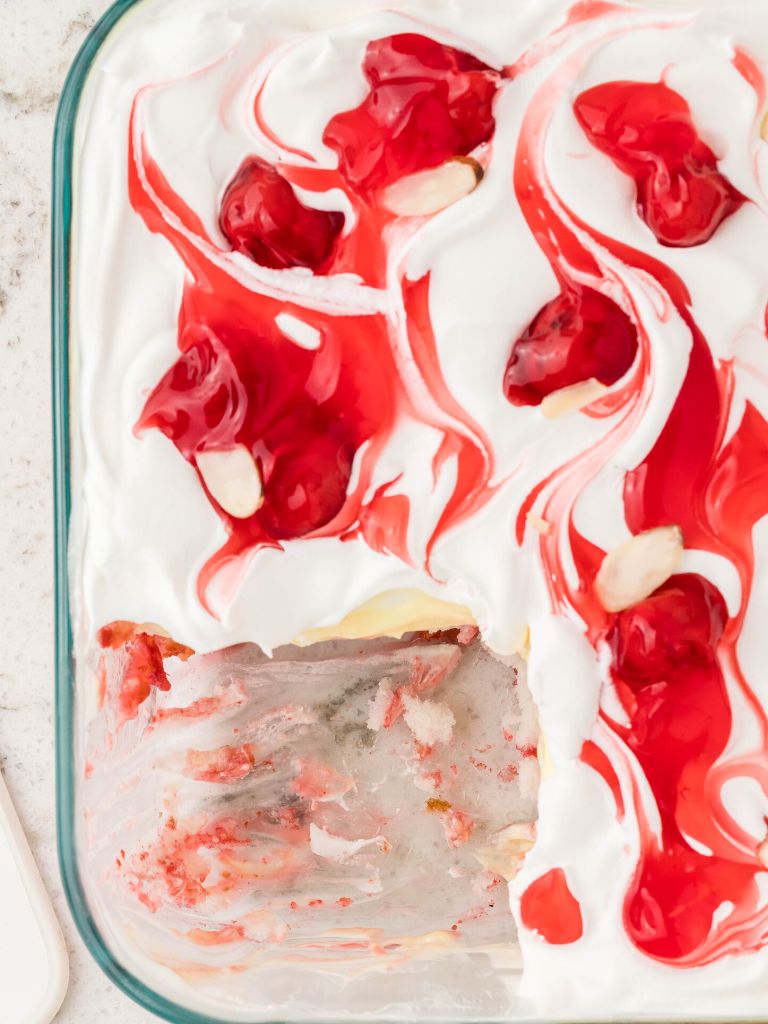Overhead picture of a cake inside a glass square pan, topped with cherry filling and cool whip. 