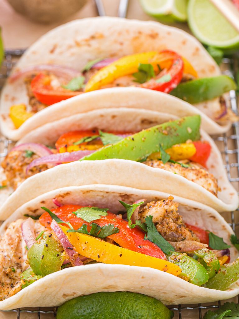 Chicken fajita mix inside flour tortillas on a cooling rack and stacked side by side. 
