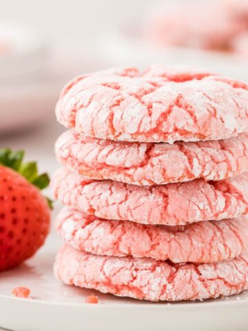 A stack of cookies with a fresh strawberry beside it.