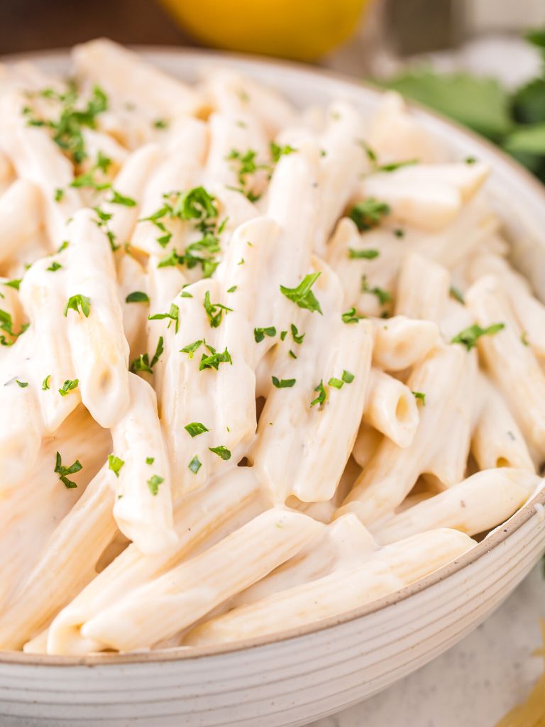 A bowl of white pasta with penne pasta and garnished with green herbs.