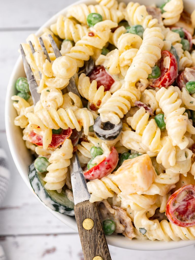 A bowl of pasta salad with a fork inside of it. 