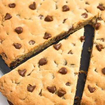 A cookie pizza with a piece cut out of it on a server spoon.