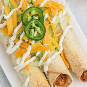 Stacked flautas topped with cheese, lettuce, and sour cream.