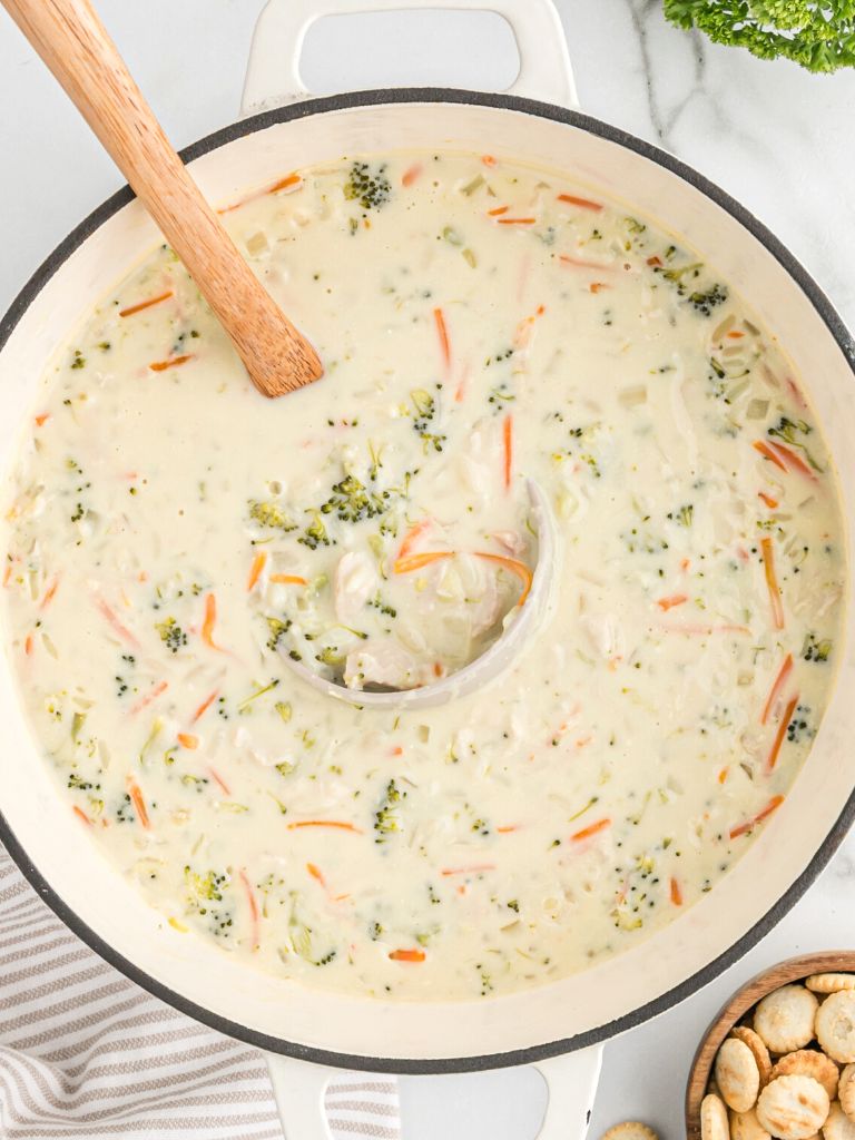 A pot of creamy soup with rice, and chicken and veggies. A soup ladle inside the pot of soup.