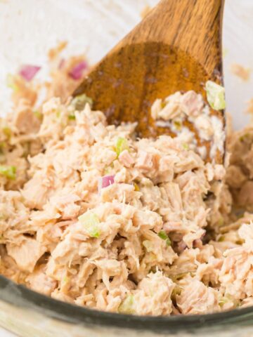 Tuna inside a bowl that is a creamy salad with a wooden spoon with some on it.