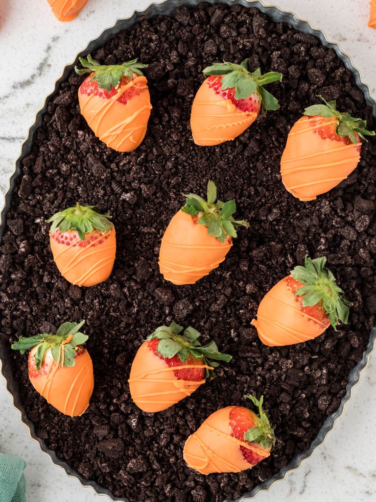 A serving platter with oreo dirt and strawberries on it that look like carrots. 