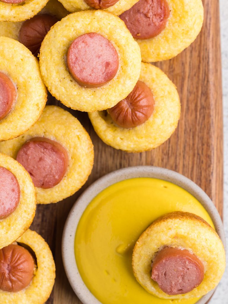 Mustard with some corn dog bites next to it. 