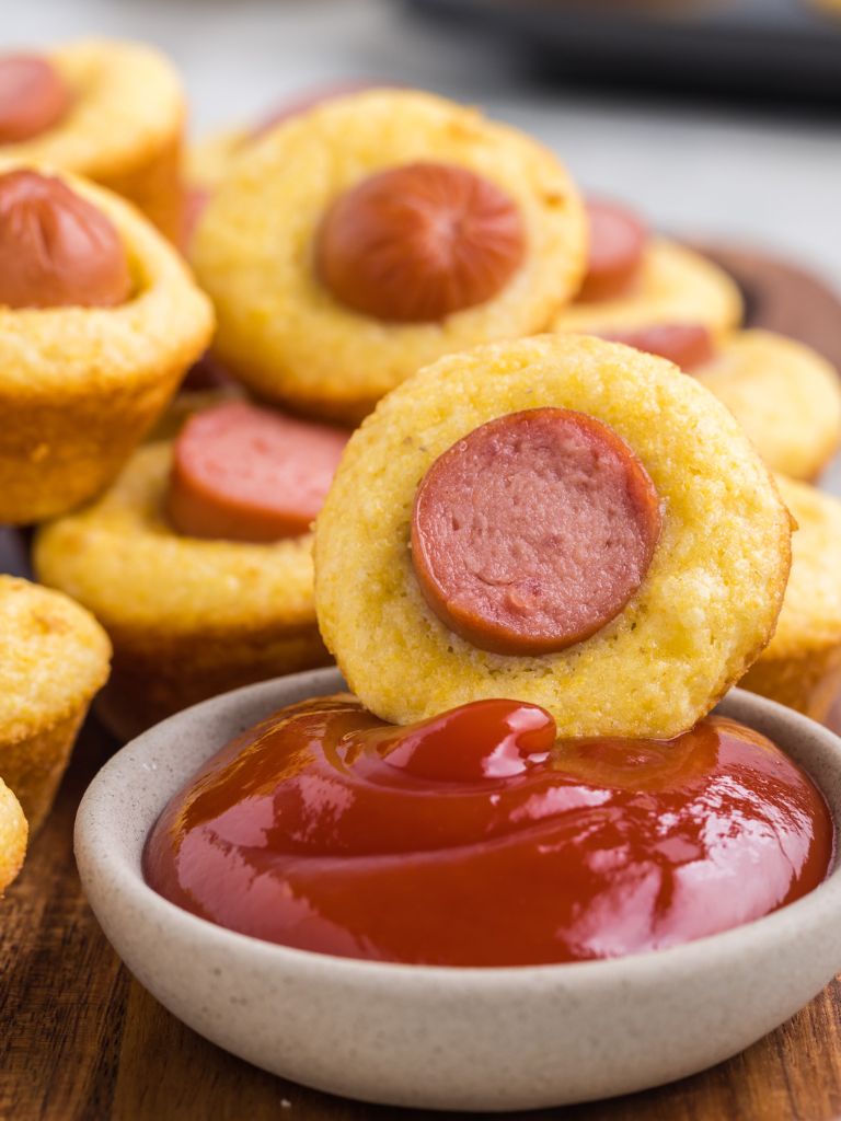 ketchup bowl with some corn dog pieces next to it. 
