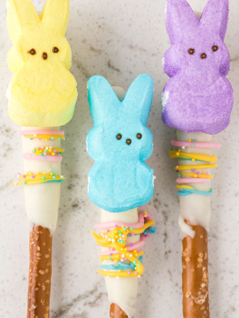 Pretzel rods laying on a white background that have been dipped in chocolate and decorated for easter.