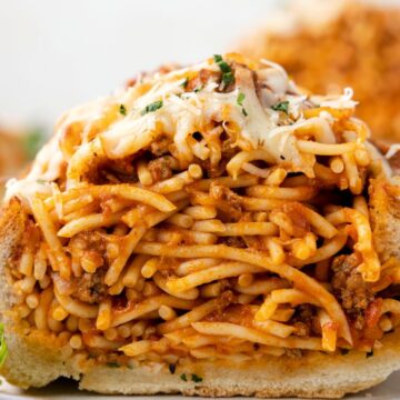 A front view of stuffed garlic bread on a white plate with spaghetti.
