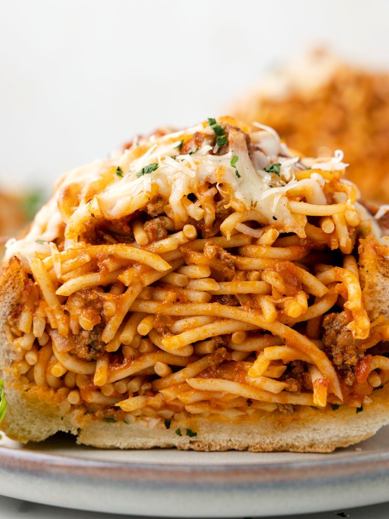 A front view of stuffed garlic bread on a white plate with spaghetti. 