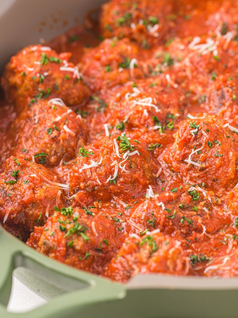 A pan of meatballs with sauce over them and parmesan cheese. 