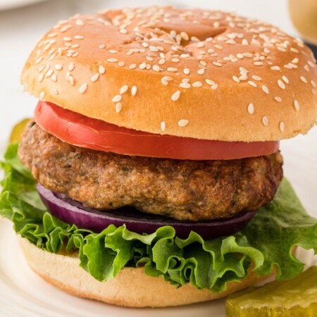 A burger with toppings sitting on a white plate inside a bun.