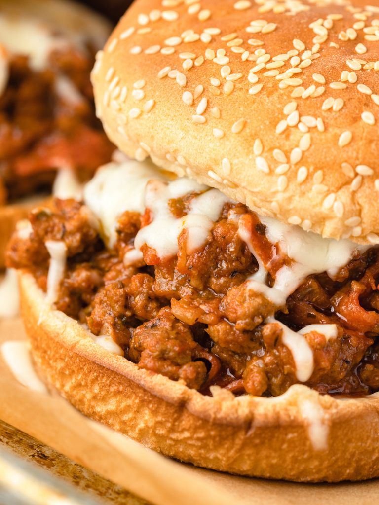A sloppy Joe with meat inside of it sitting on a piece of parchment paper. 