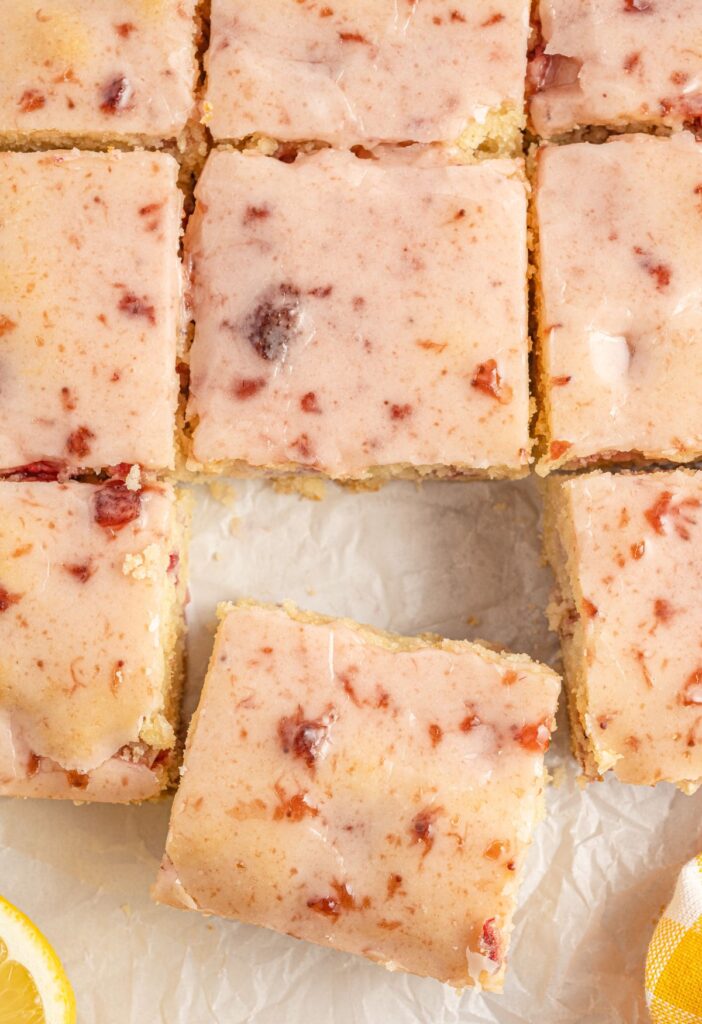 Blondies with a jam glaze cut into squares next to lemon slices. 