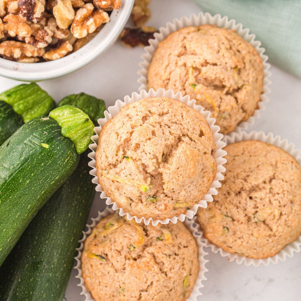 Overhead shot of several muffins with walnuts and whole zucchini next to them.
