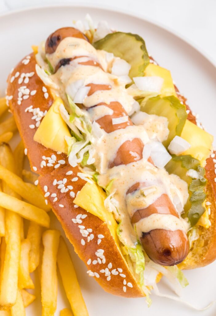 A hot dog on a white plate with French fries.