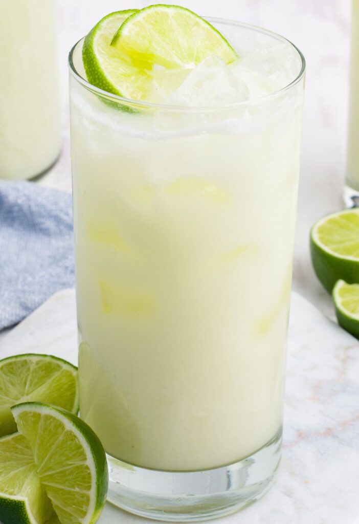 A glass of this lemonade drink garnished with limes and ice on top. 