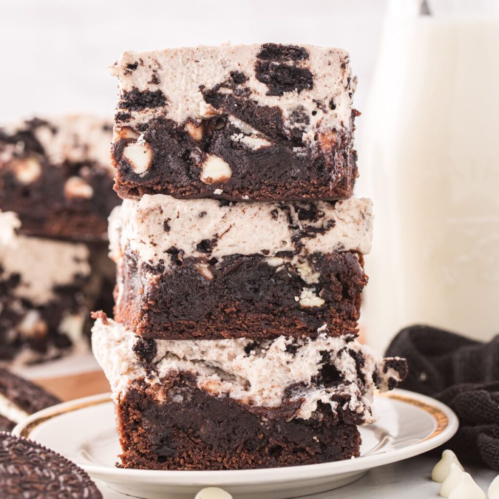 A stack of brownies with a glass of milk in the background. 