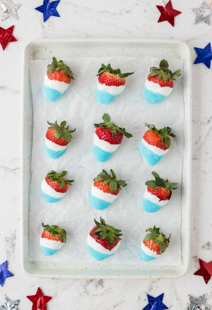 Dipped strawberries in red, white, and blue on a baking sheet. 