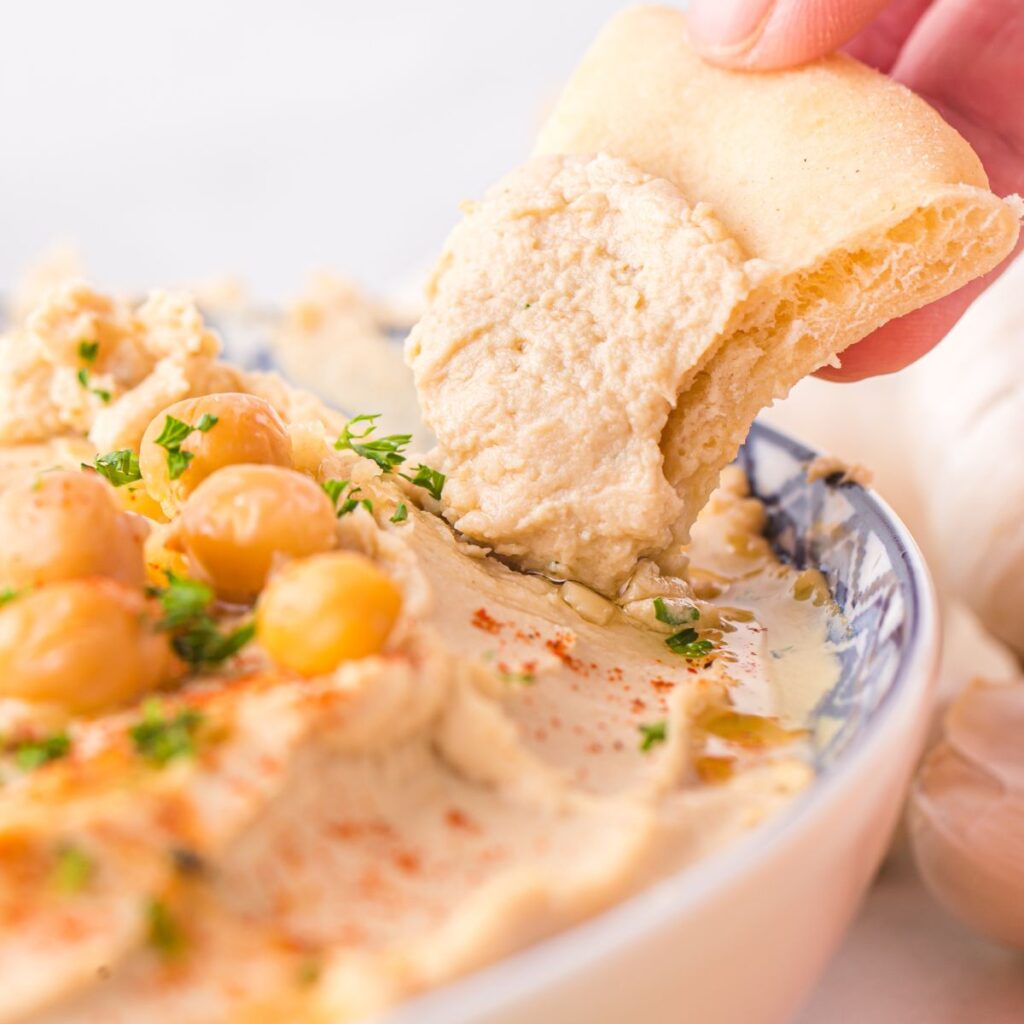 A hand holding a piece of bread dipping it into the dip. 
