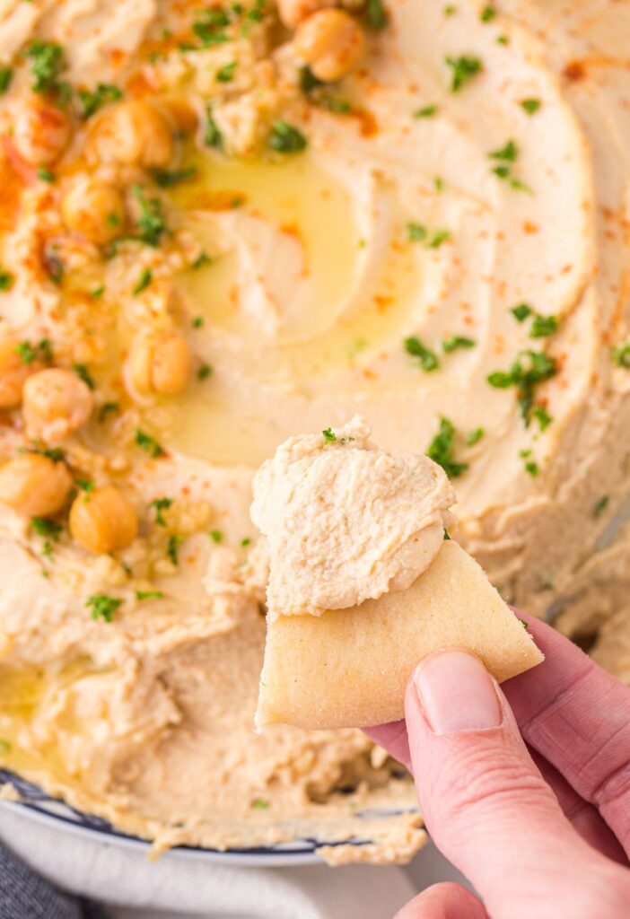 A hand holding a pita chip dipping it into the hummus.