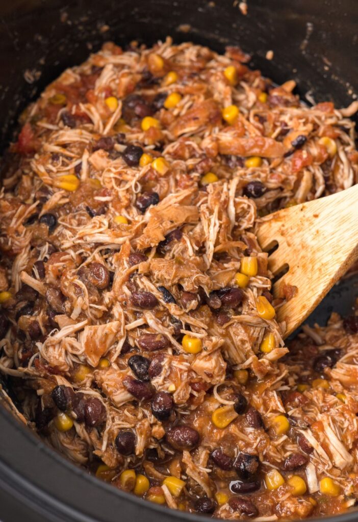Chicken taco meat inside the slow cooker with a wooden serving spoon.