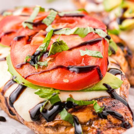 A close up of this grilled chicken with tomato, avocado, and basil.