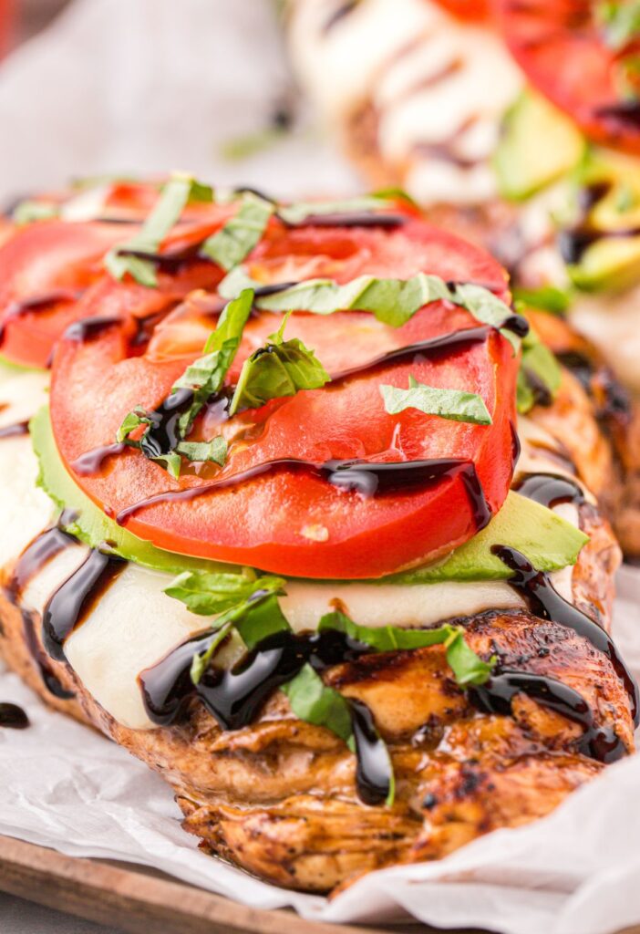 A close up of this grilled chicken with tomato, avocado, and basil.