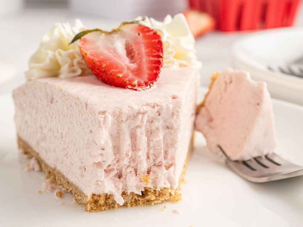 A serving of cheesecake with a fork with a bite on it. 