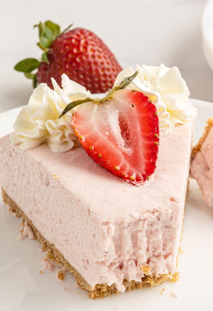 A slice of cheesecake topped with a strawberry and a bite taken out the front with a fork. 