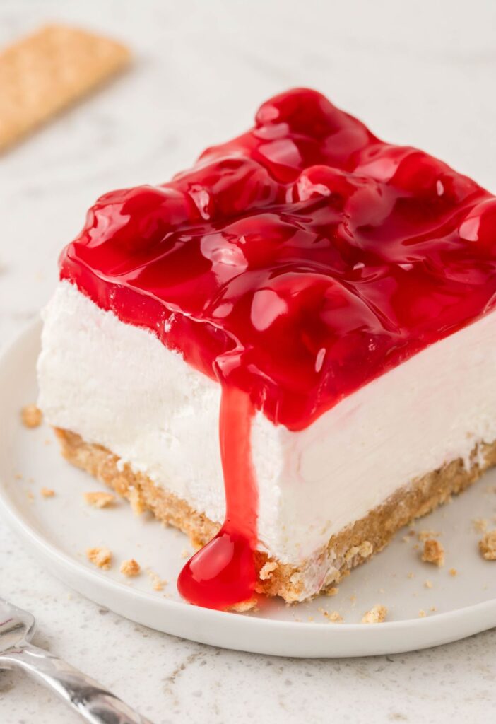 A slice of this no bake desert with cherry sauce spilling over the edge.