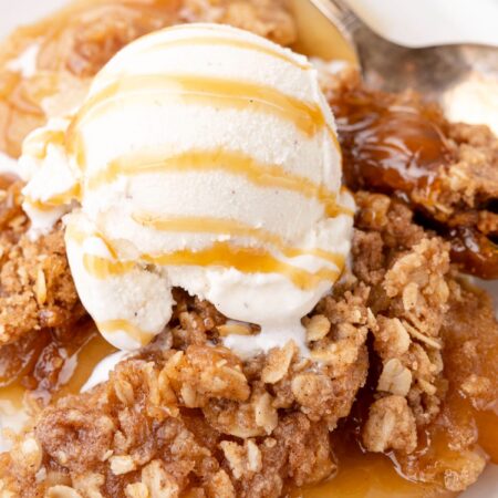 Served warm apple crisp on a white plate with ice cream on top.