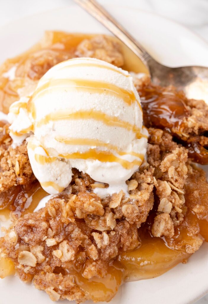 Served warm apple crisp on a white plate with ice cream on top. 