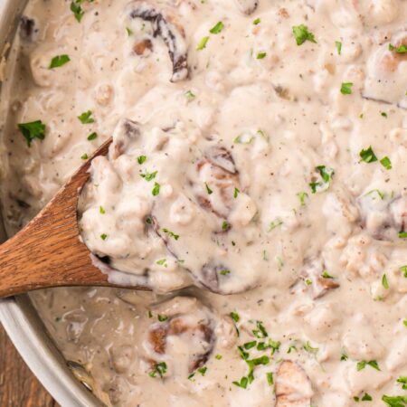 A skillet pan of creamy stroganoff sauce with a wooden spoon inside of it.