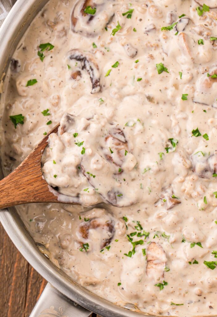 A skillet pan of creamy stroganoff sauce with a wooden spoon inside of it. 