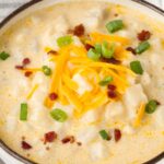 a bowl of chunky potato soup inside a bowl with toppings.