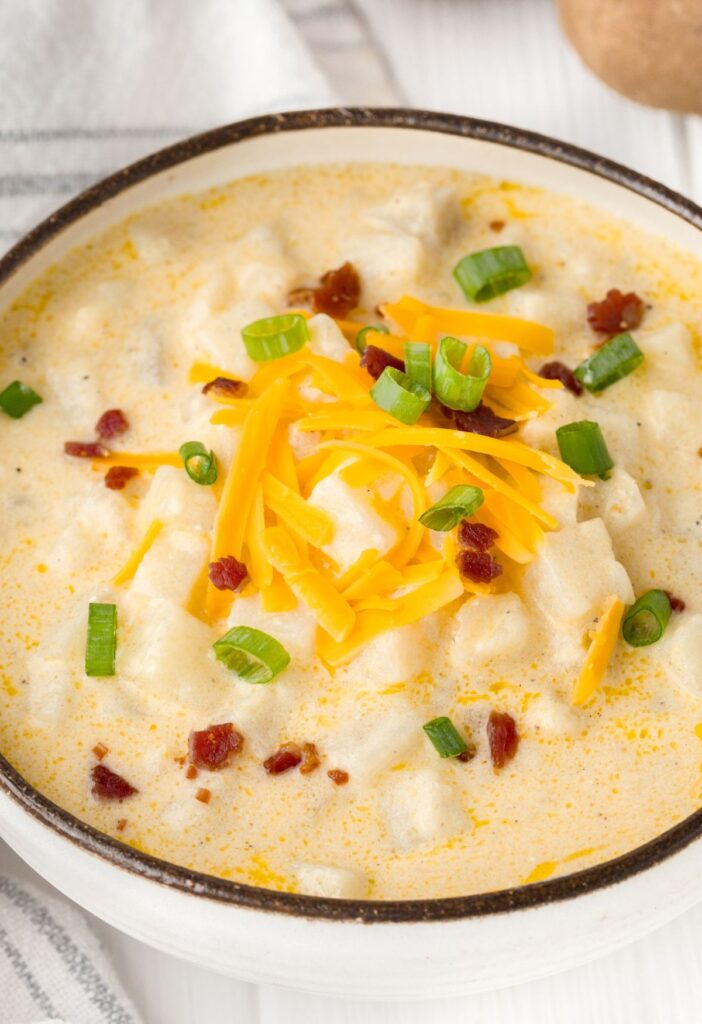 a bowl of chunky potato soup inside a bowl with toppings.
