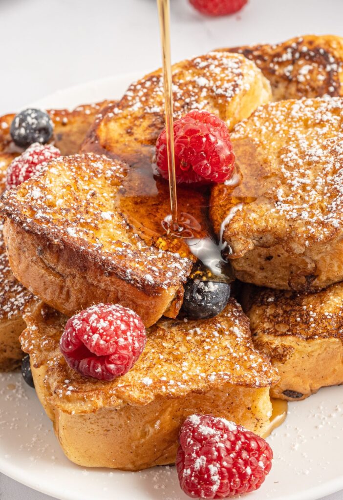 A stack of cooked French toast on a plate with berries. 