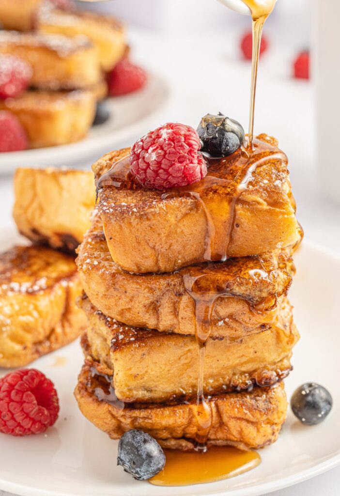 A stack of French toast rolls with berries and syrup. 