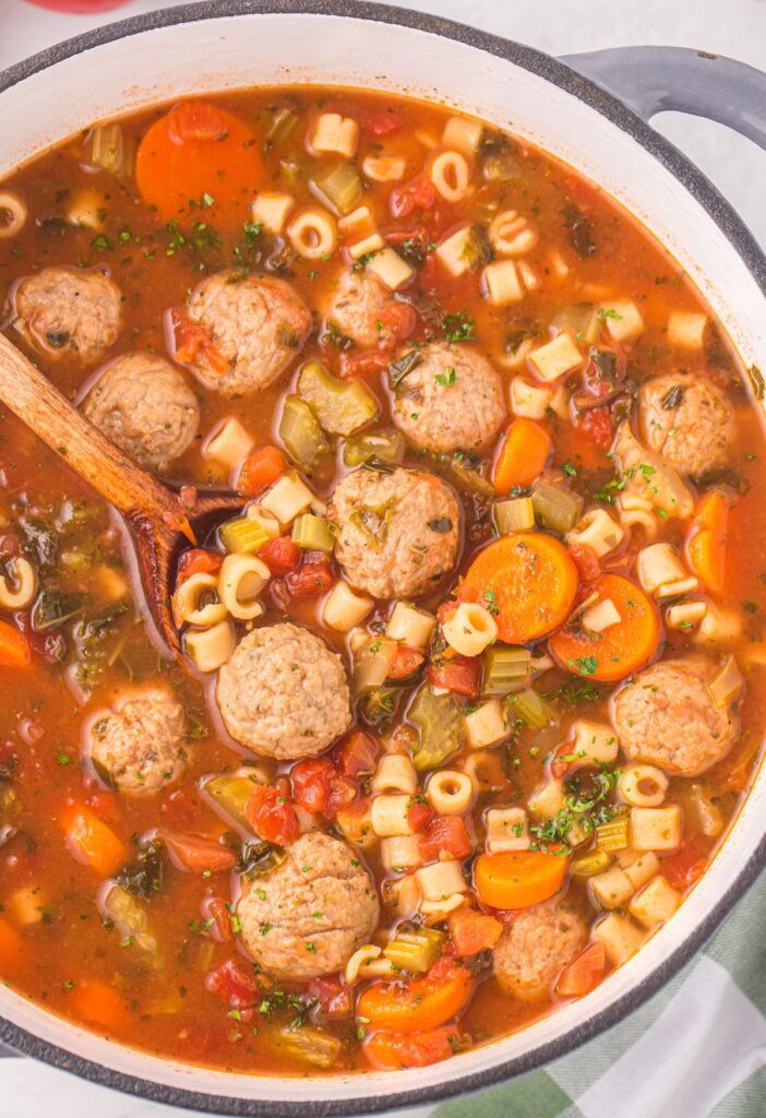 A soup pot of this meatball soup with a wooden spoon inside of it for serving. 