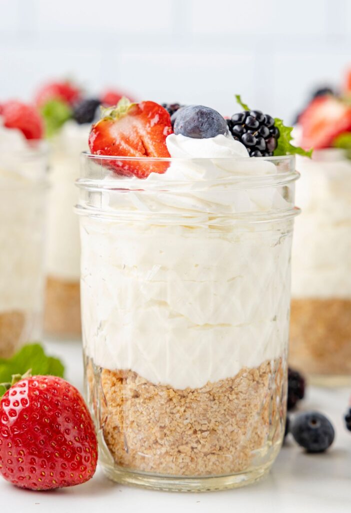 A jar of crust, cheesecake, and topped with berries. 